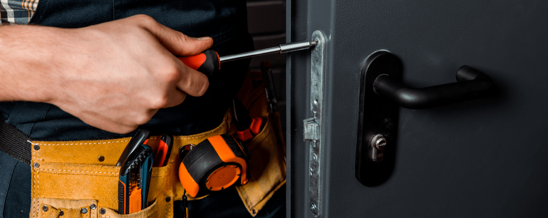 A closeup of an engineer's hands and the side of a door as they use a screwdriver to screw a lock faceplate into position